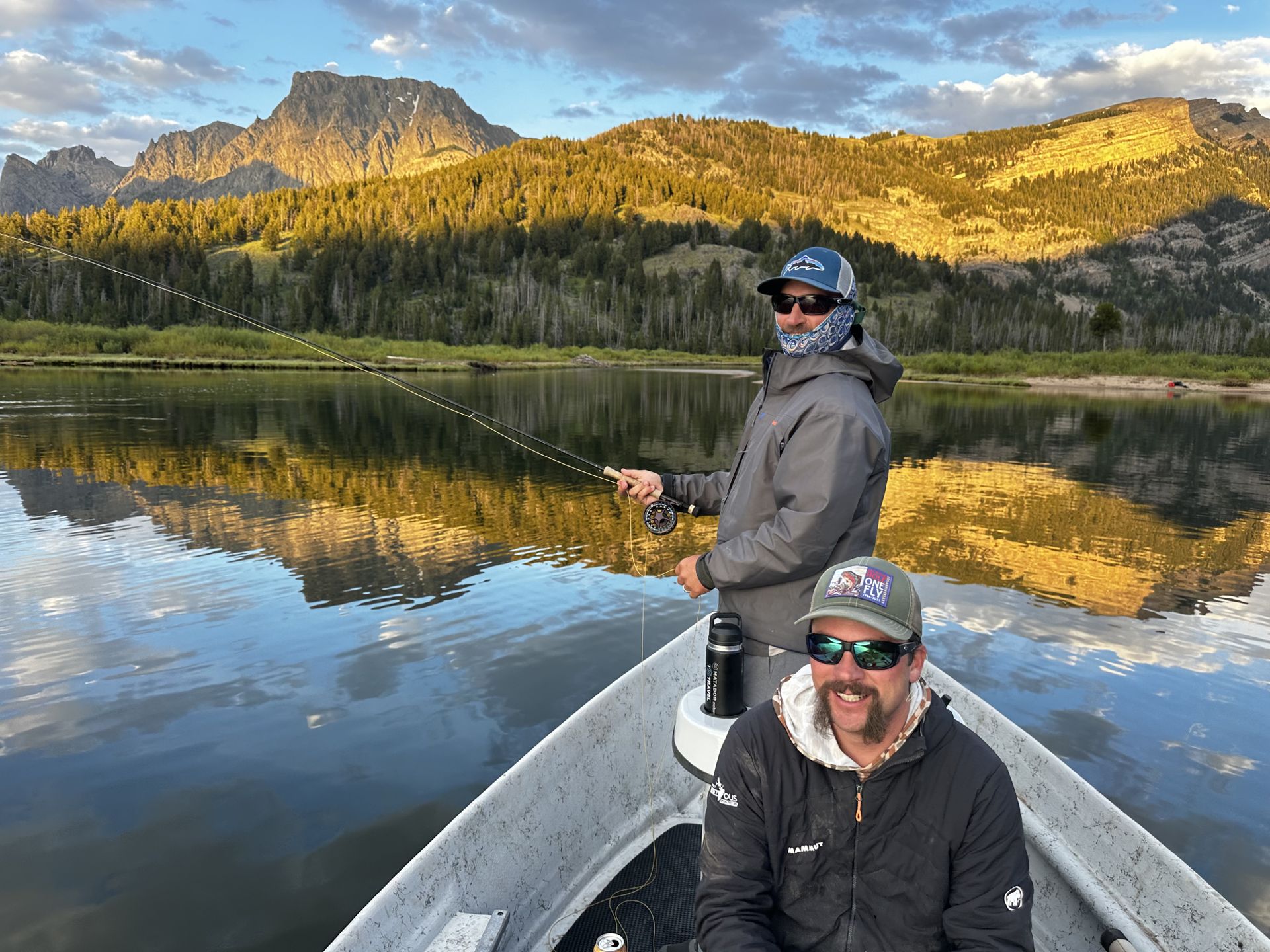 Two people in a canoe on a calm lake with mountain reflections at sunrise