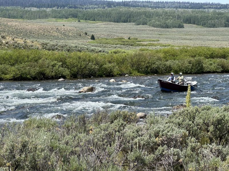Small raft with two people on a fast river amid green wetlands and open tundra-like plains