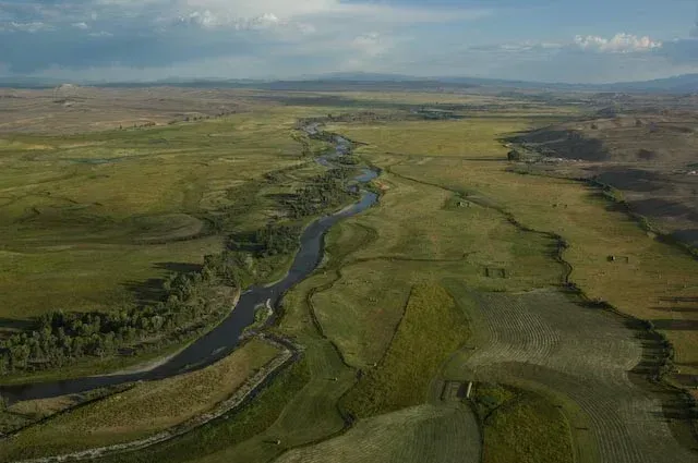 A winding river cuts through green and brown fields under a cloudy sky.