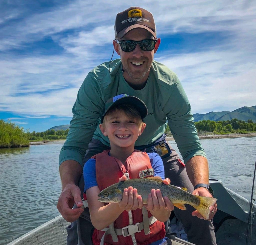 Smiling adult and child in a boat holding a fish on a sunny lake