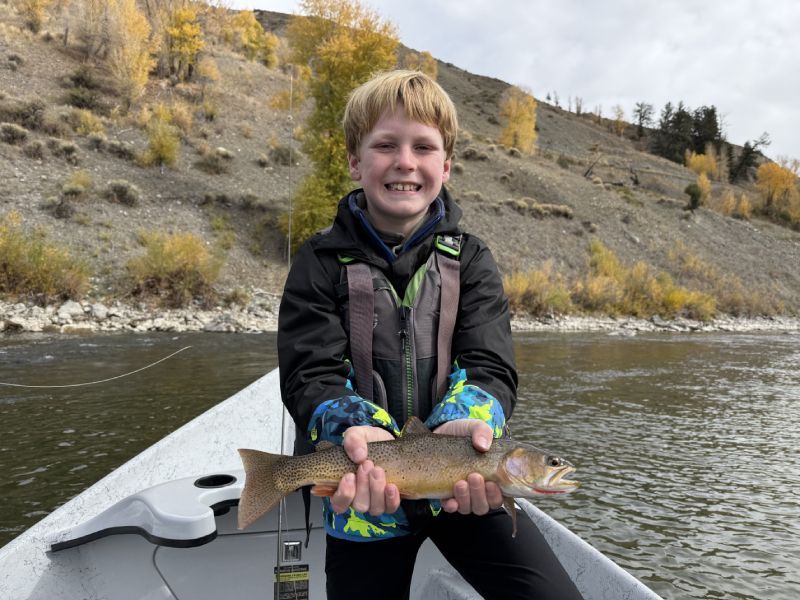Smiling child on a boat holding a fish on a river with autumn hills in the background