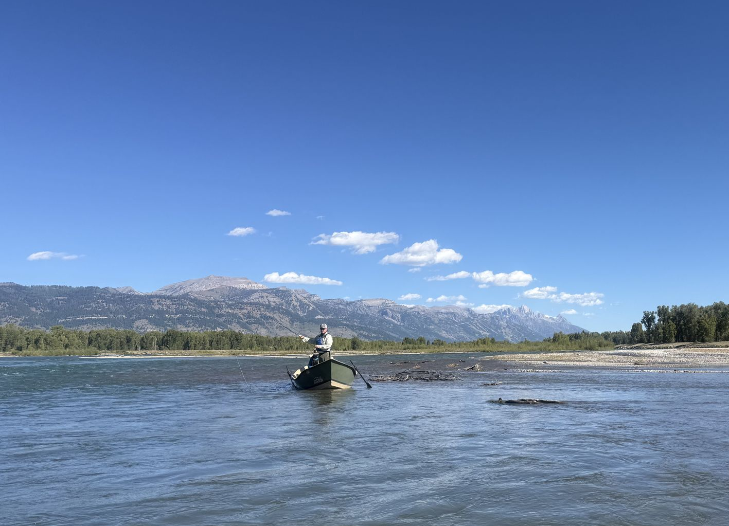 Three people fishing from a small boat on a river with green hills in the background