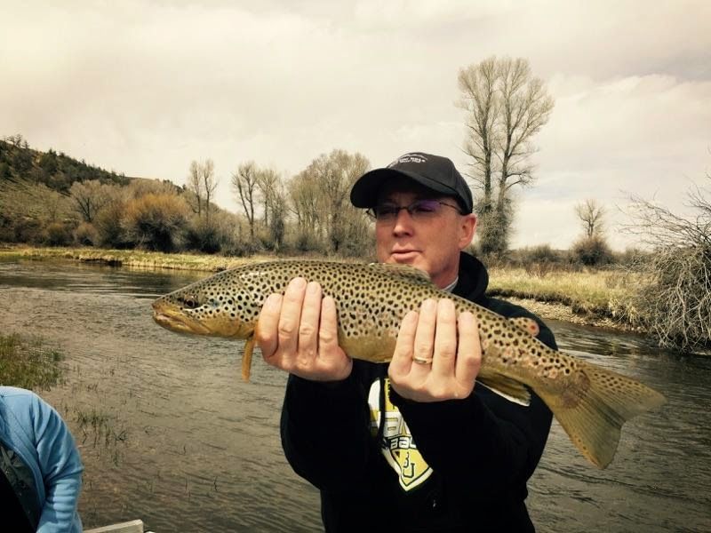 Person holding a large spotted fish in a river under an overcast sky