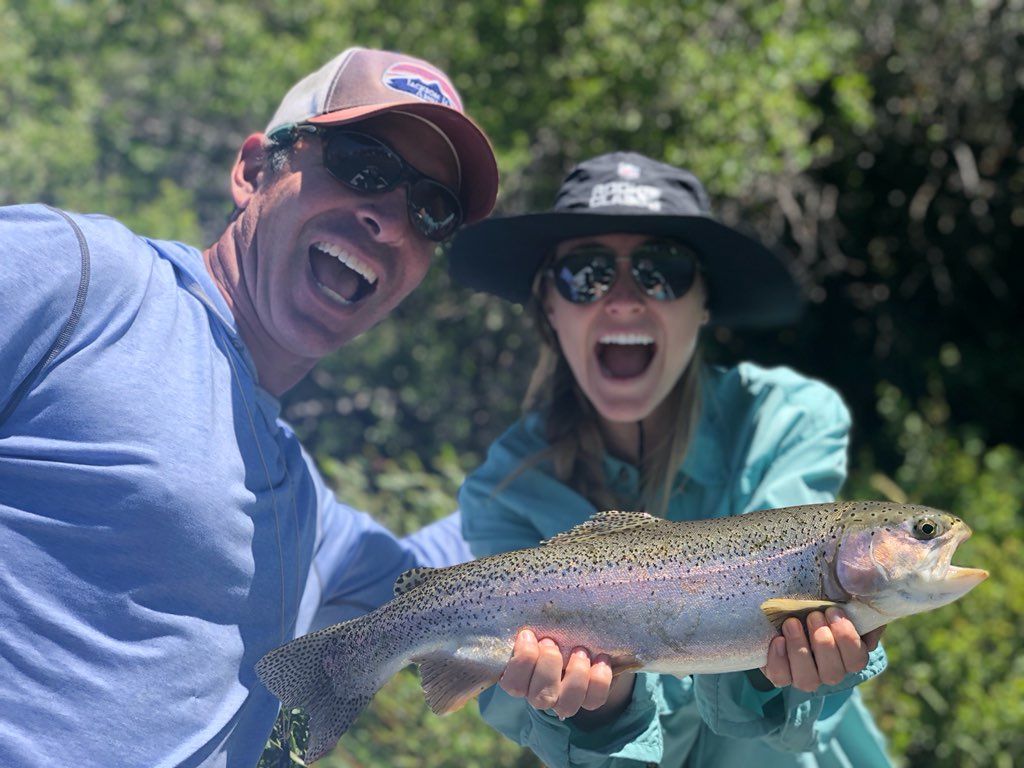 Two smiling people holding a large rainbow trout outdoors