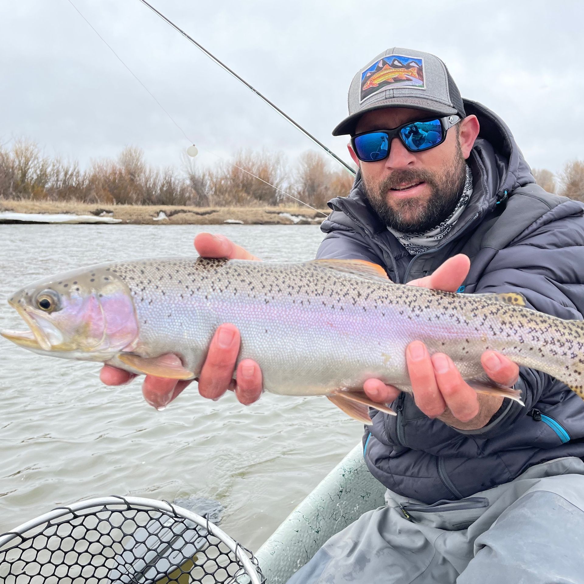 Angler in a boat holding a silvery trout with pink spots over a river
