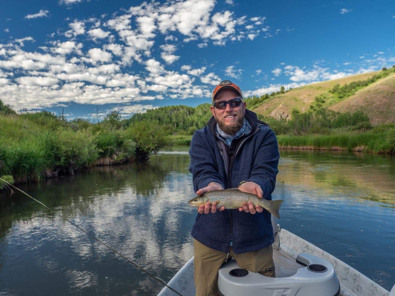 Man holding a fish on a boat in a calm river under a blue sky
