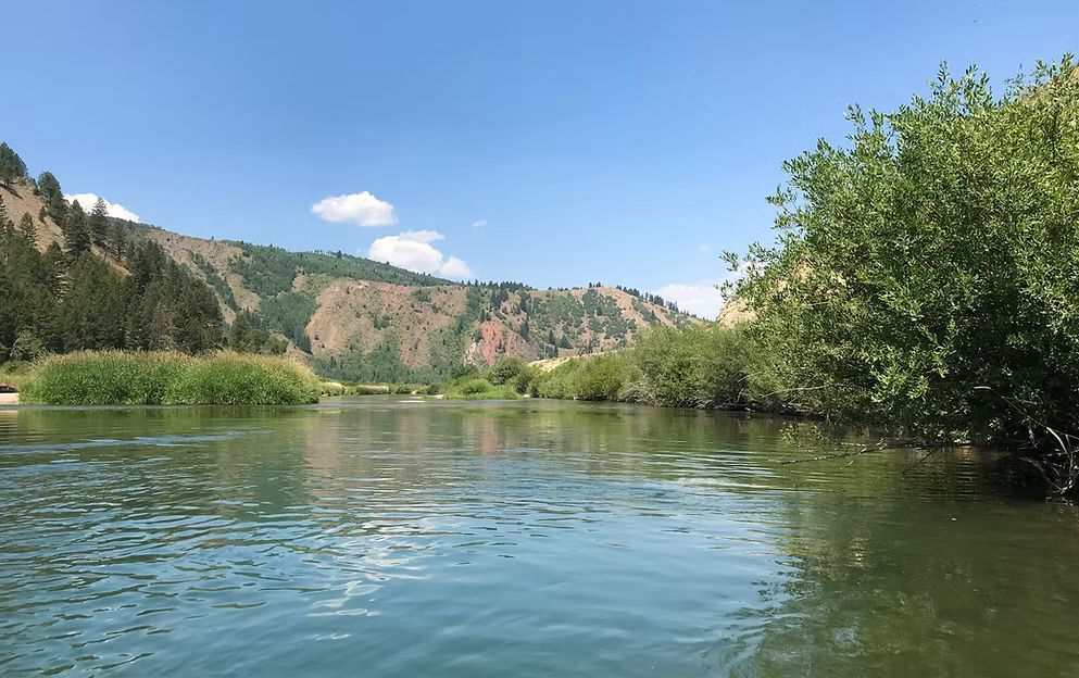 Calm river with green banks, rocky hills, and clear blue sky on a sunny day