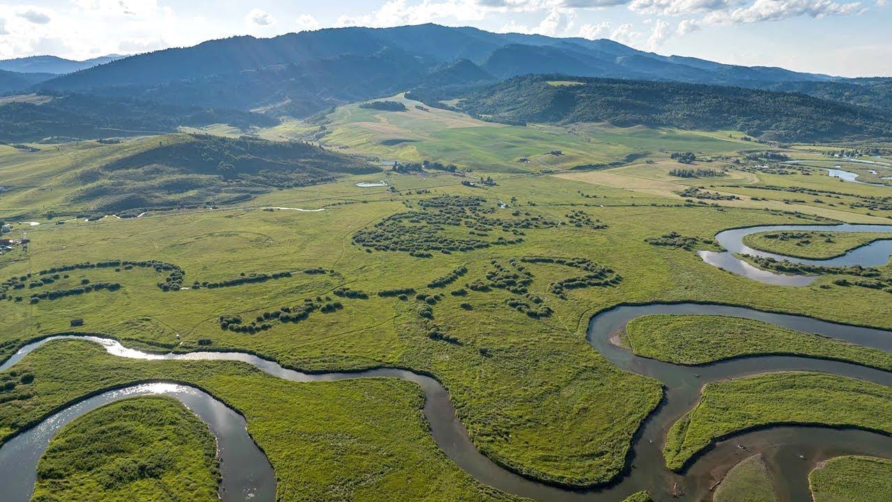 Winding river through green wetlands with mountains in the distance under a clear sky