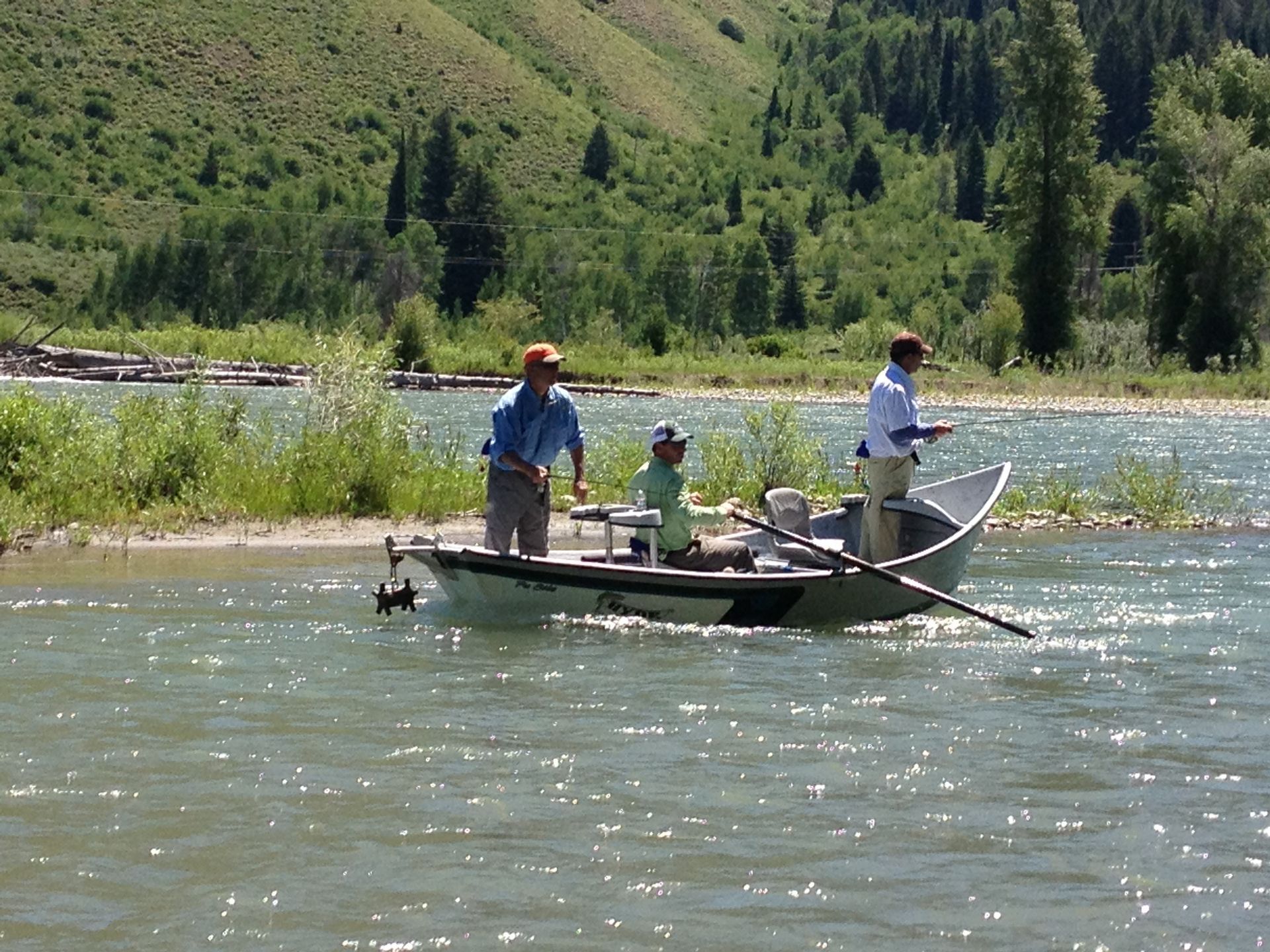 People fishing from a small boat on a calm river with green hills in the background