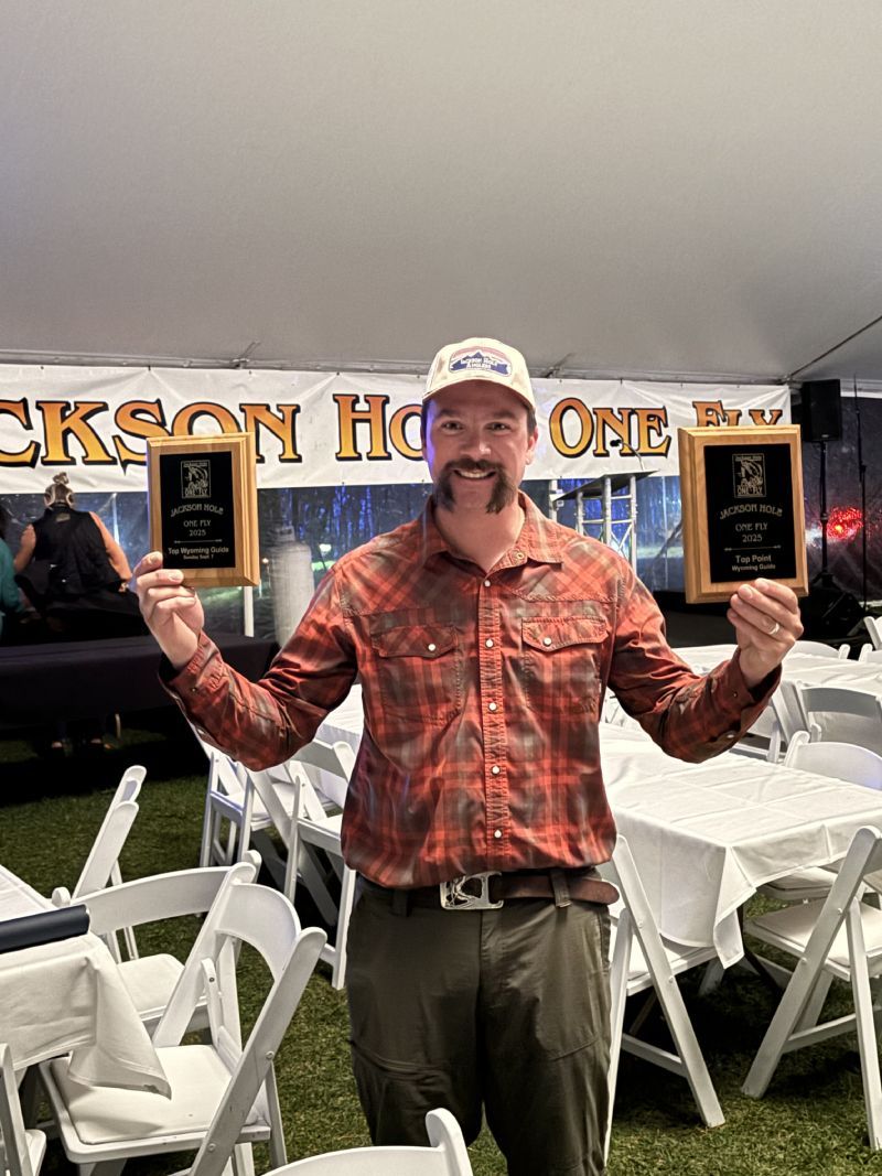 Man holding two plaques in front of a Jackson Hole banner at an outdoor banquet table