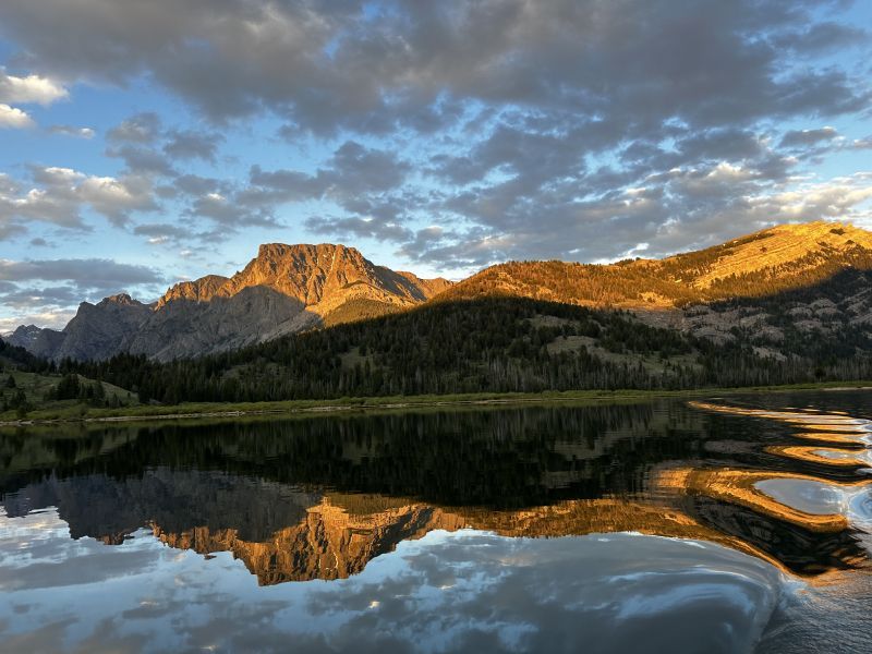 Sunlit mountain range reflected in a calm lake under a partly cloudy sky