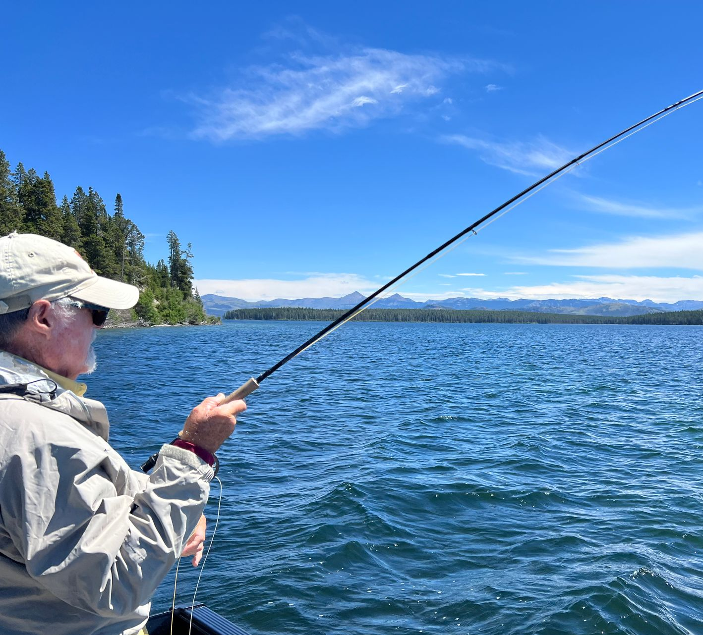 Man holding a large fish on a boat, wearing a straw hat and green shirt on a river with forest behind