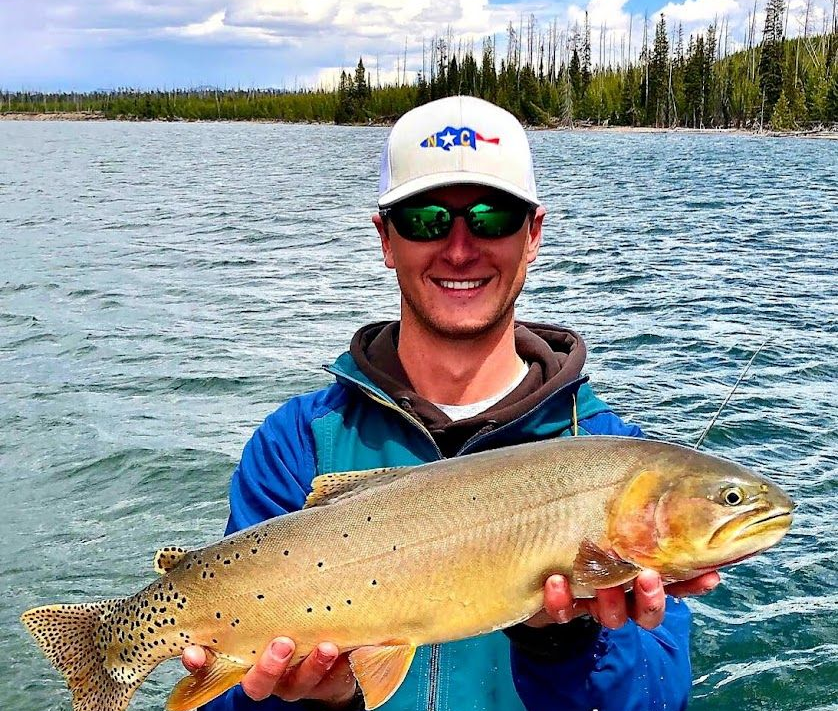 Angler smiling and holding a large fish on a boat with lake and forest in the background