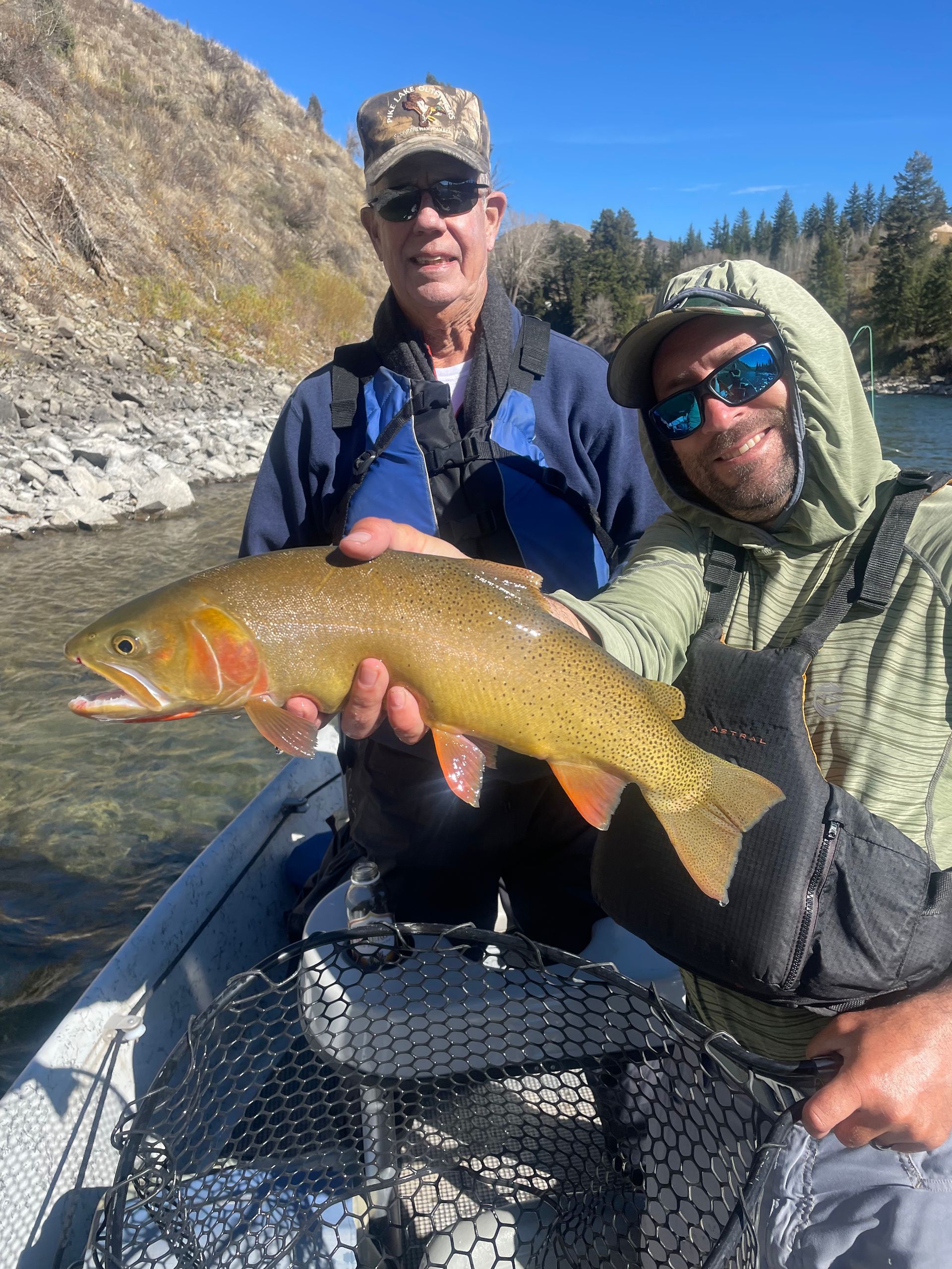 Two anglers in a boat holding a large golden fish on a mountain river