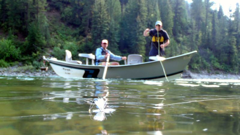 Two people in a small boat on a calm lake, with a forested shoreline in the background.