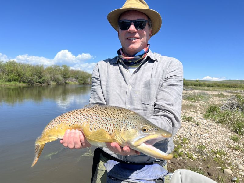 Angler holding a large fish by a calm river under a blue sky