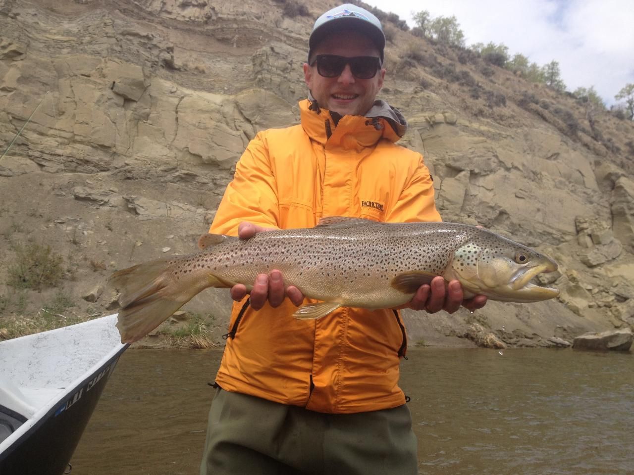 Angler in an orange jacket holding a large fish beside a riverbank