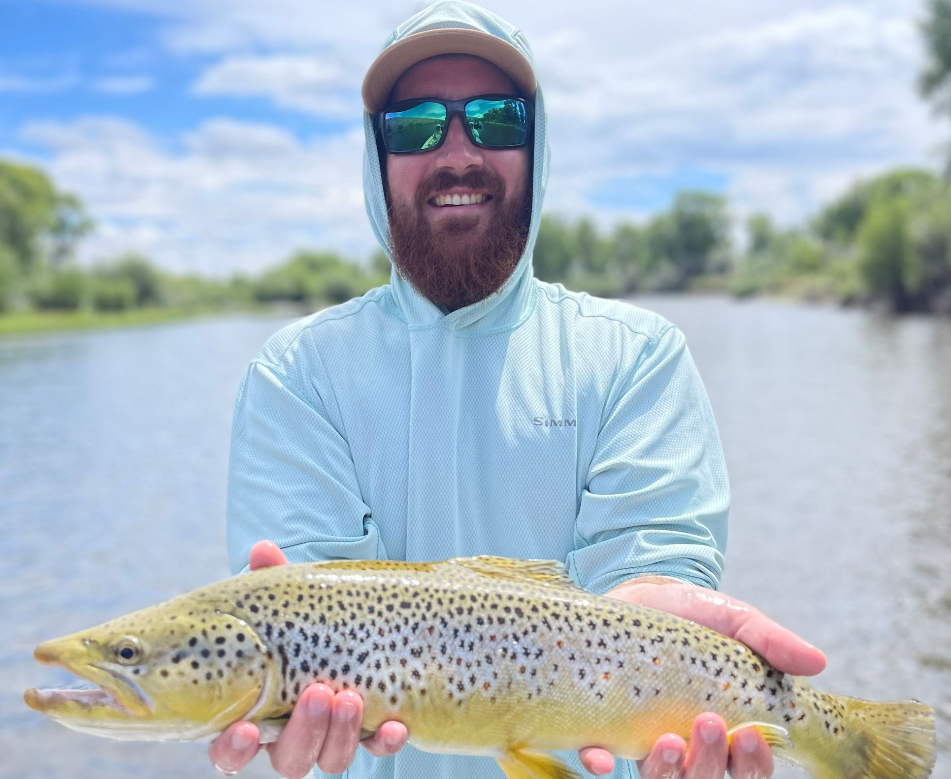 Angler holding a spotted fish beside a river under a cloudy sky