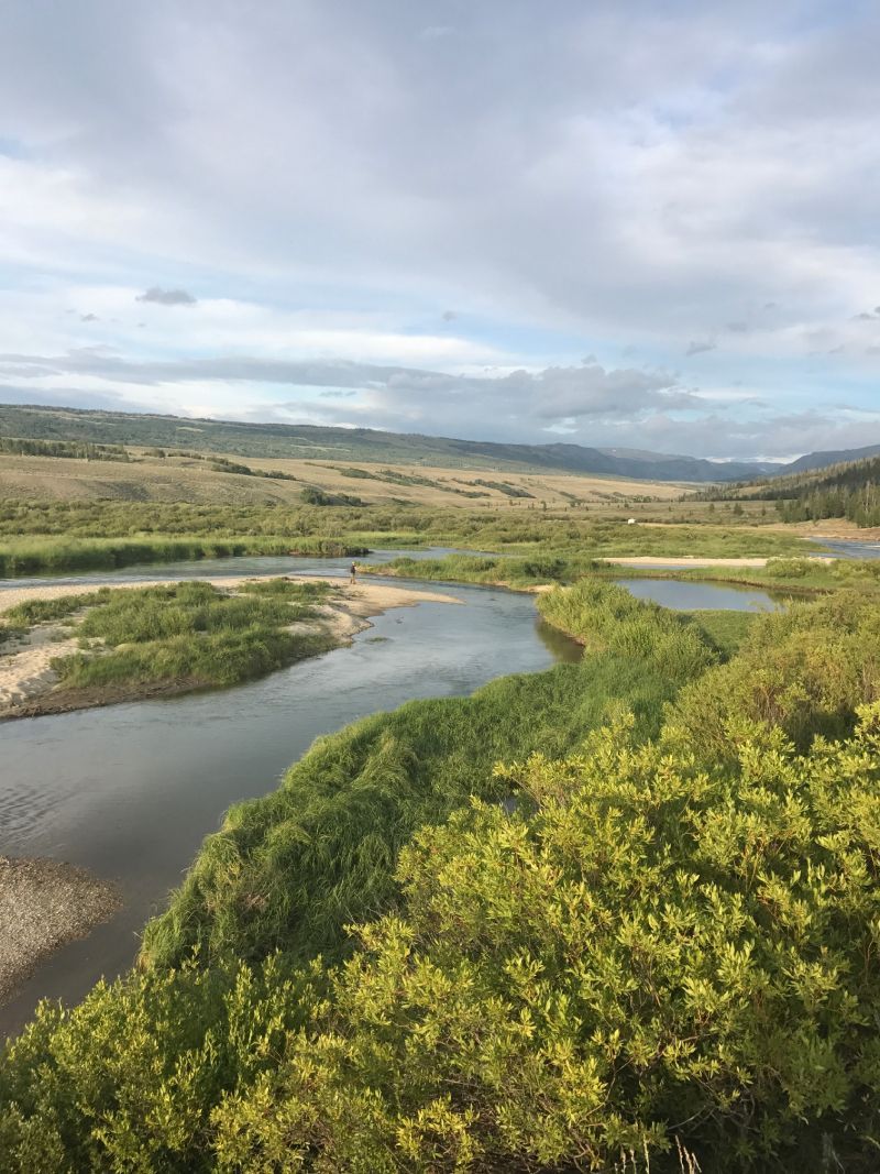 Wide river winding through a green valley under a cloudy sky with distant hills