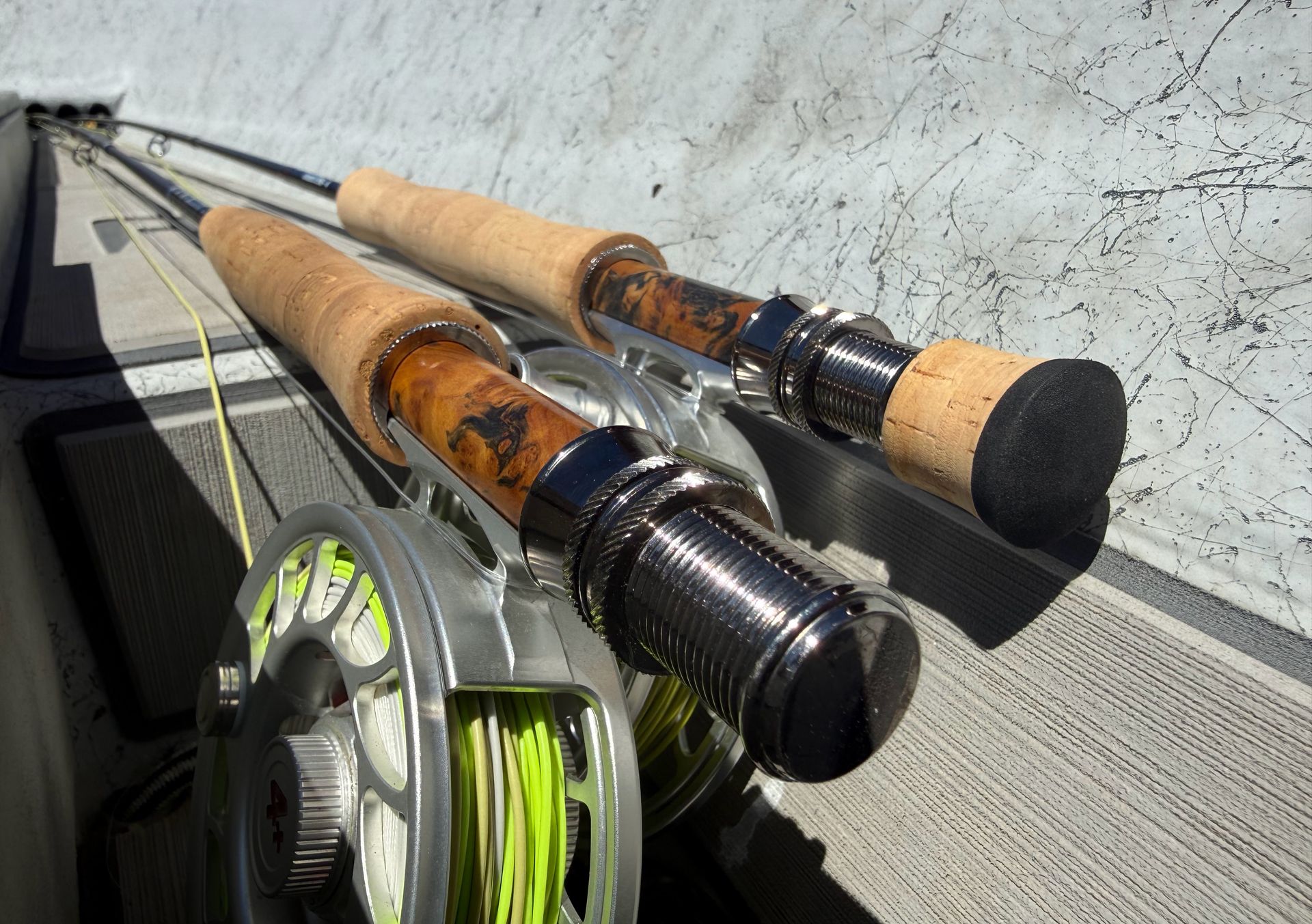 Fly fishing rods and reels laid on a concrete ledge in bright sunlight