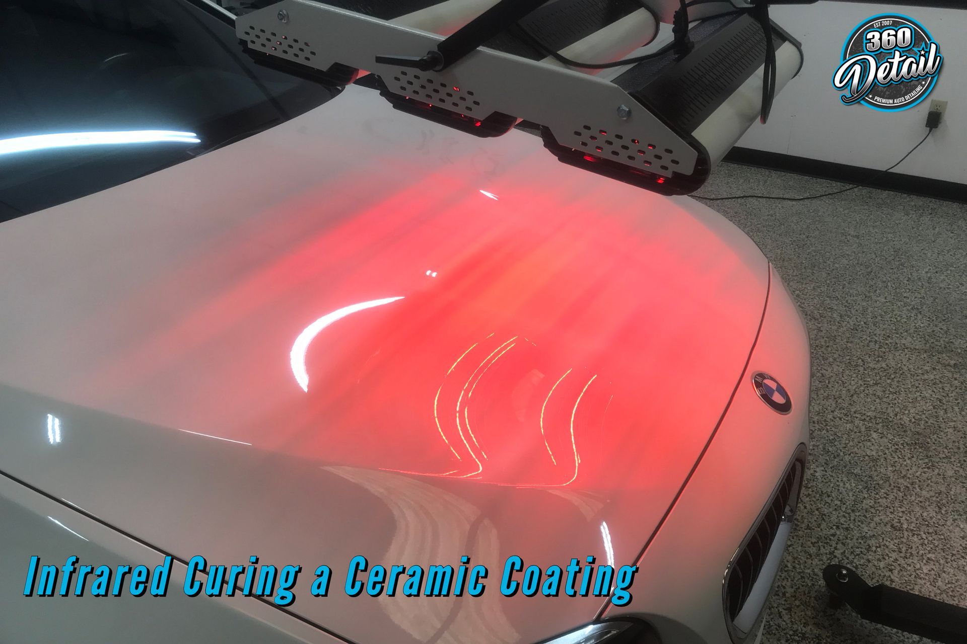 Infrared curing ceramic coating on a white car hood, glowing red. Garage setting.