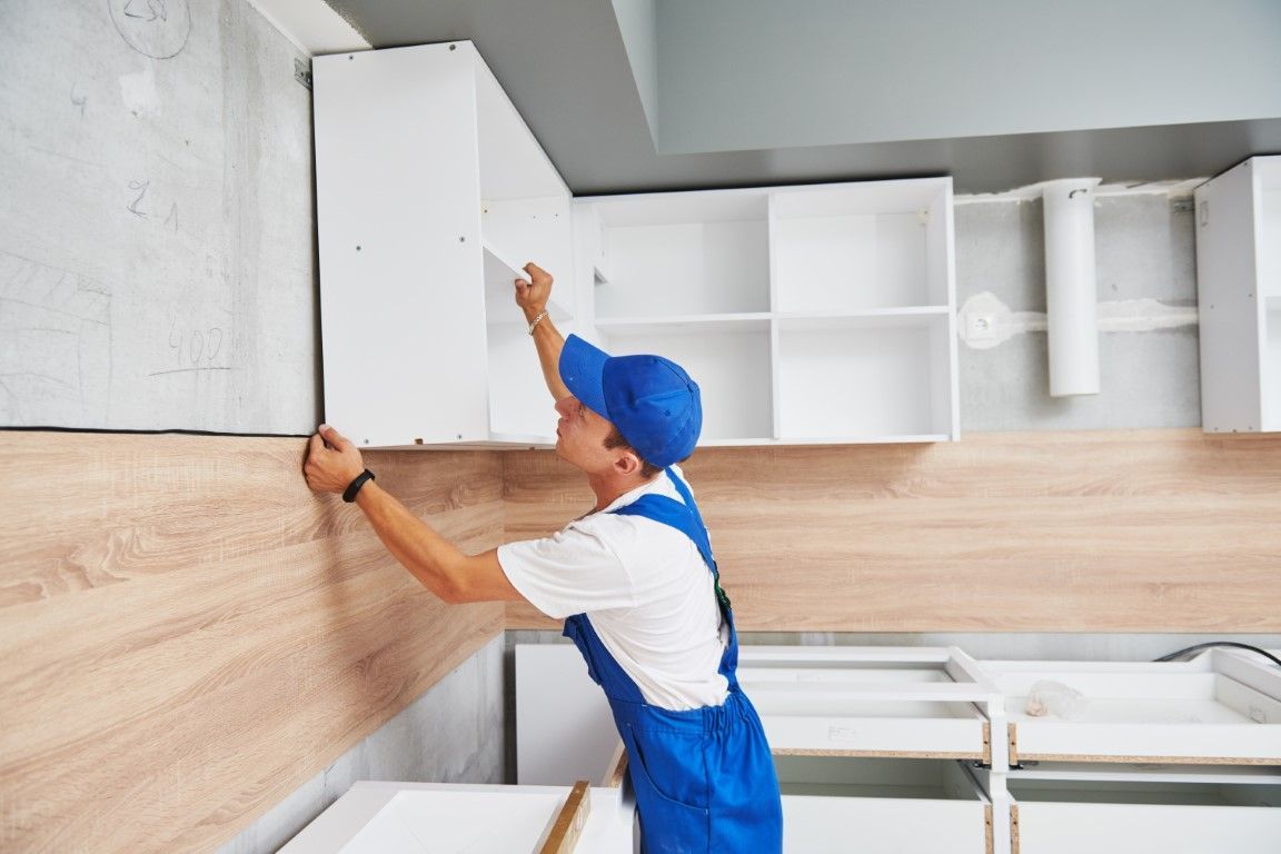 Worker installing white cabinets and a wood backsplash in a kitchen under renovation
