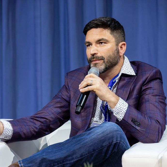 A man in a purple jacket is sitting in a chair holding a microphone