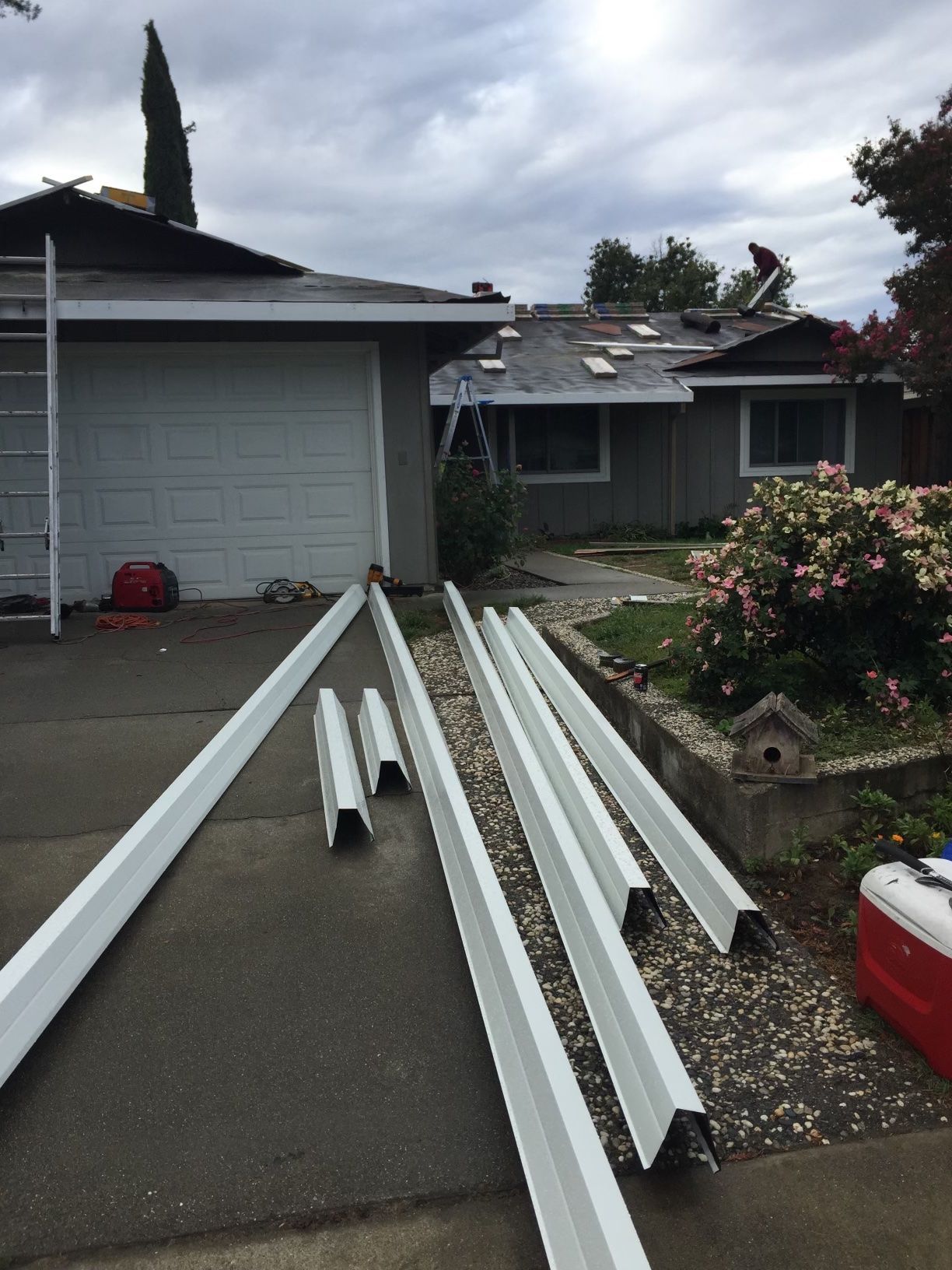 White gutter sections and trim pieces laid out on a driveway outside a house after storm damage.