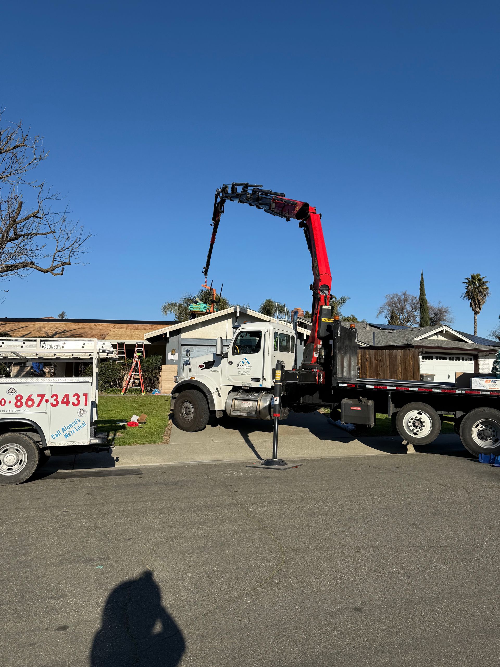 White crane truck lifting debris over a flatbed trailer in a sunny parking lot