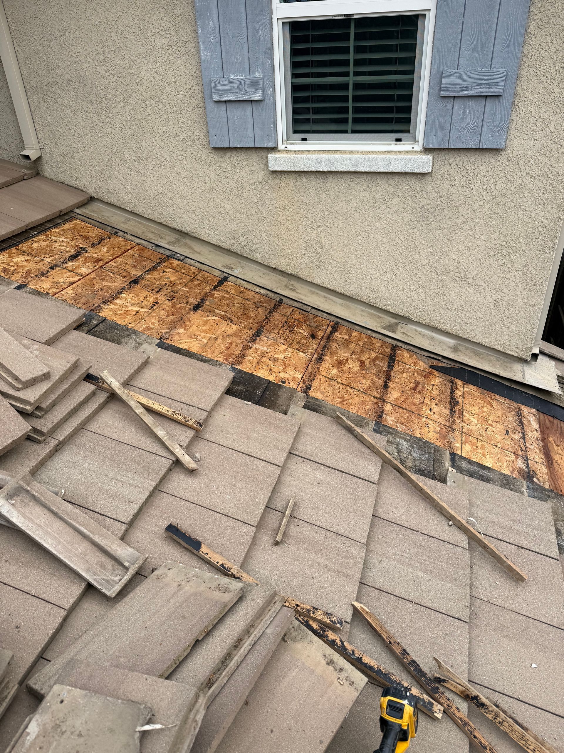 Roof shingles removed below a window, exposing wood sheathing and underlayment during repair