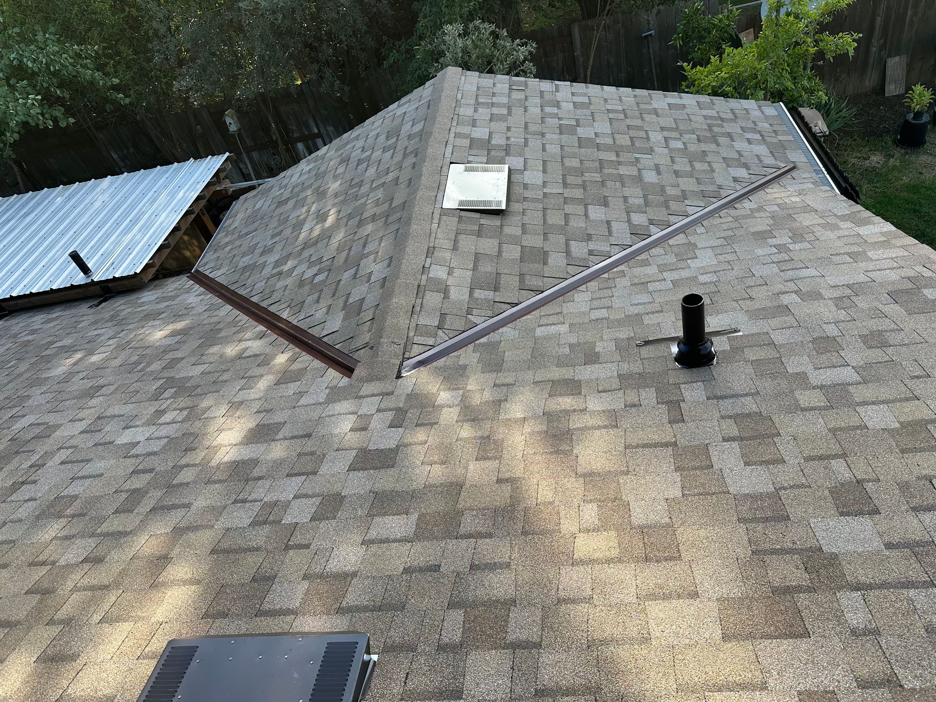 Roof shingles with multiple vents and skylights, viewed from above in a wooded area