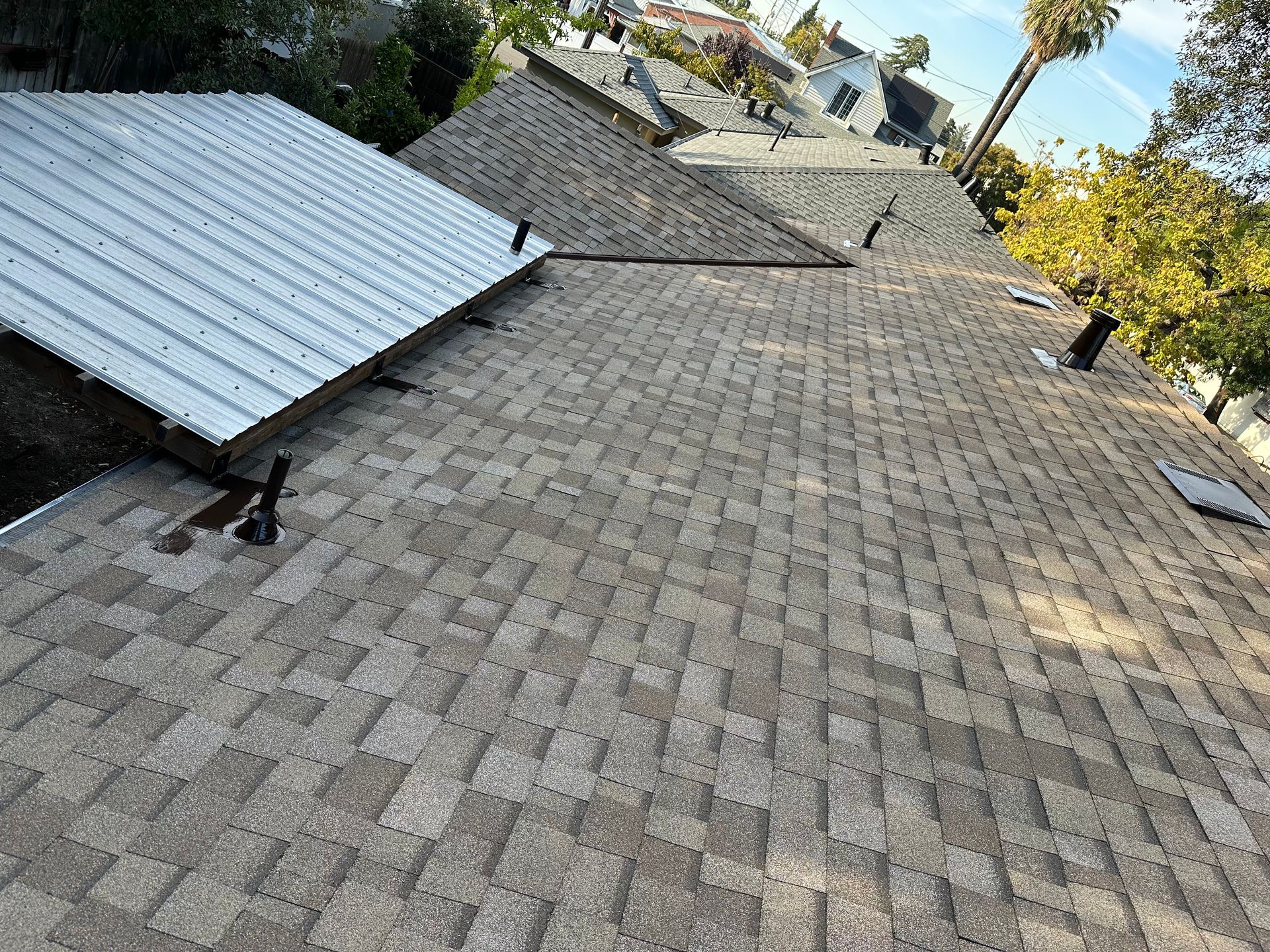 Roof with gray shingles and a white metal roof section on a house in a residential area