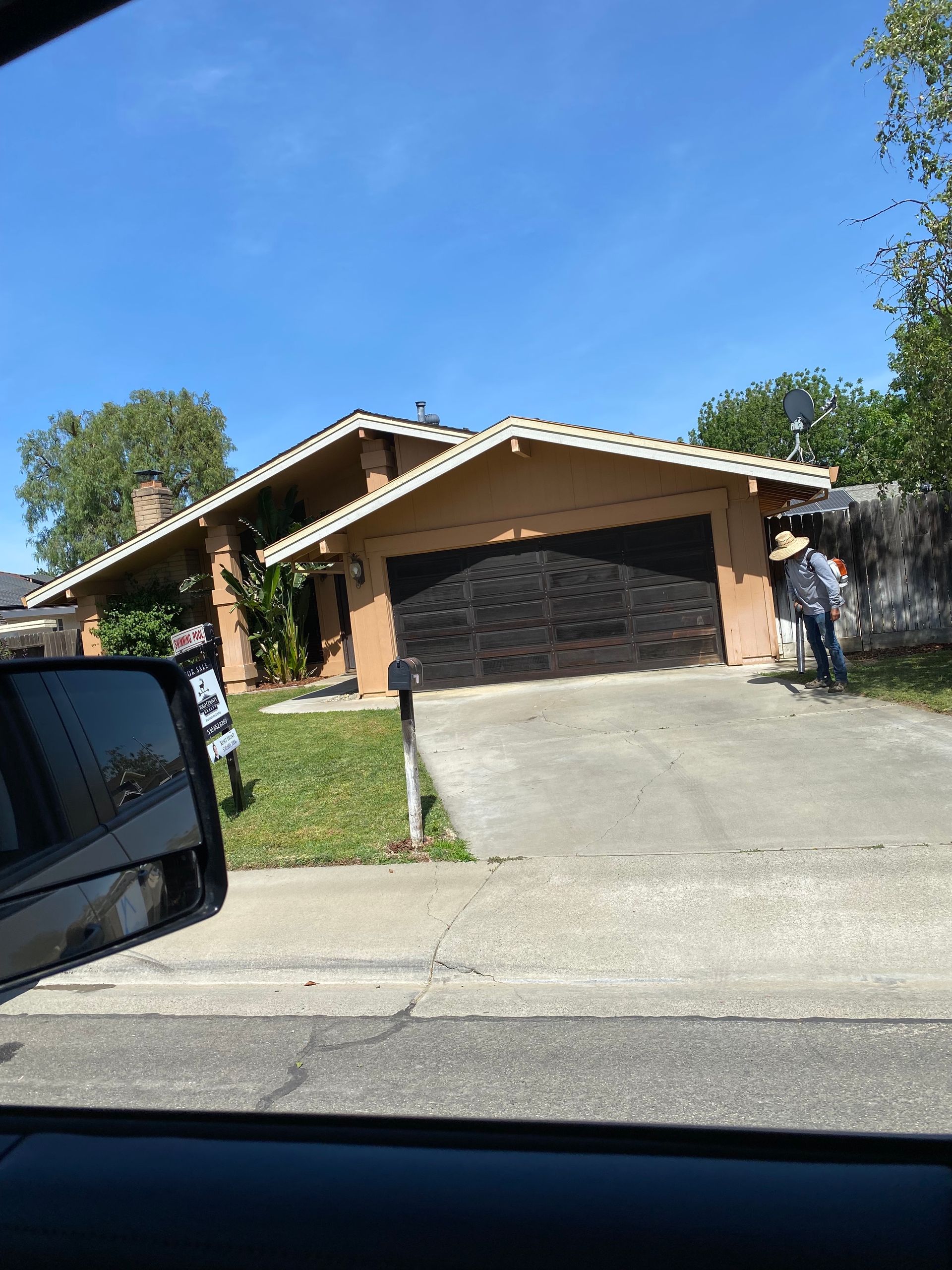 Suburban house with a brick facade and driveway under a clear blue sky, seen from inside a car.