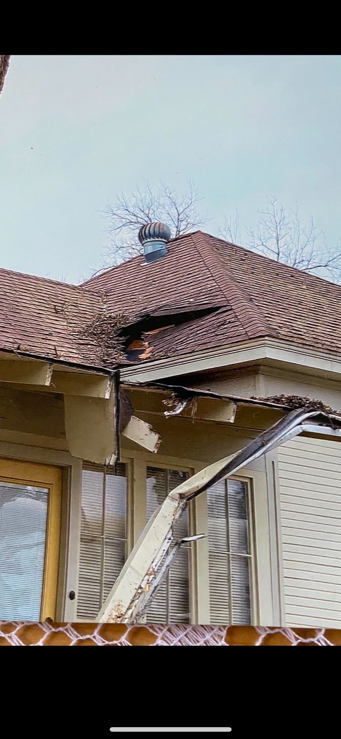 Damaged house roof with a large hole and broken shingles under a cloudy sky