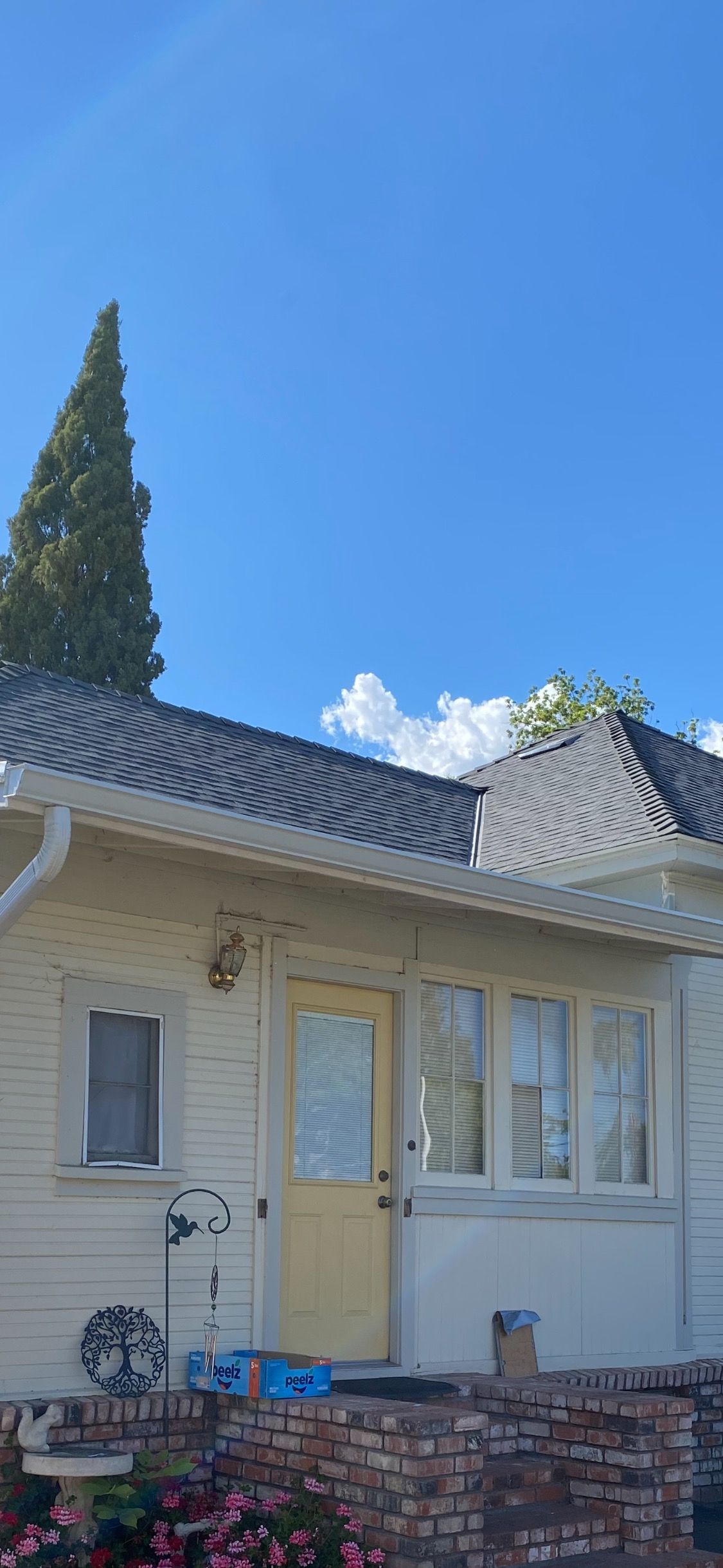 Cream-colored house with white shutters, a tiled roof, and a brick planter under a bright blue sky.