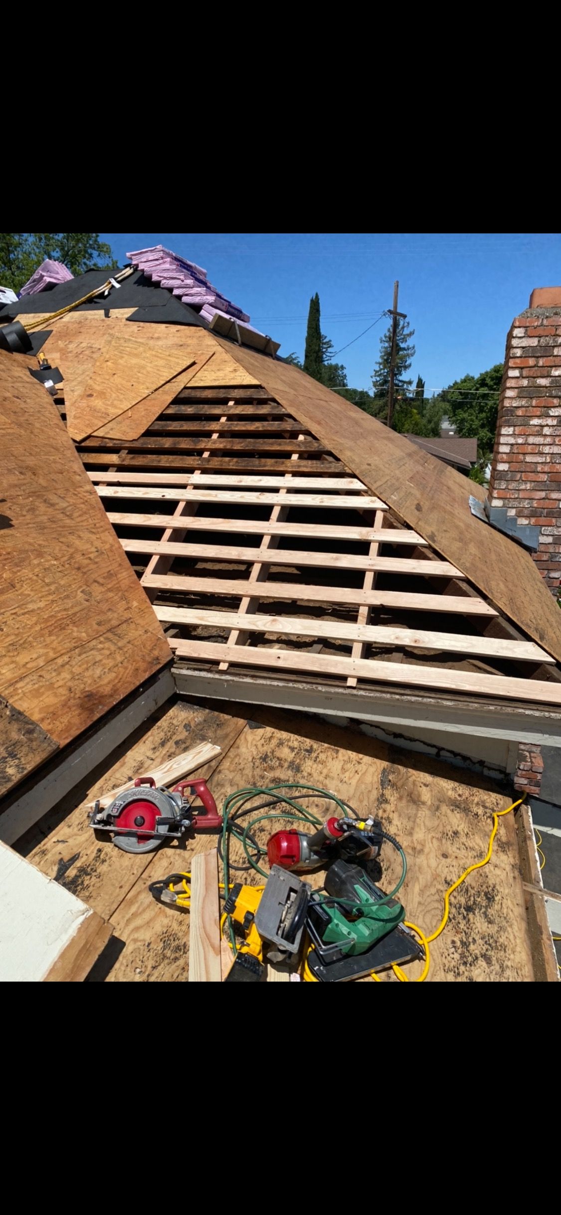 Roof under construction with exposed rafters, shingles, and tools on a sunny day
