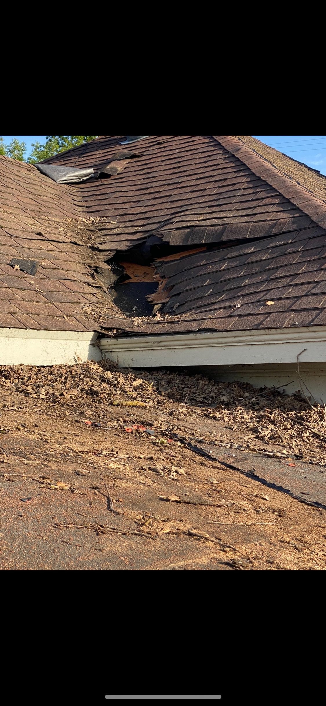 Damaged shingled roof with exposed wooden structure and debris under a blue sky