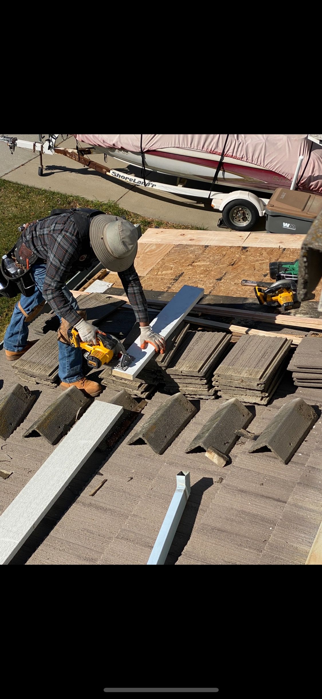 Worker using a hammer to repair roof shingles beside a parked truck.