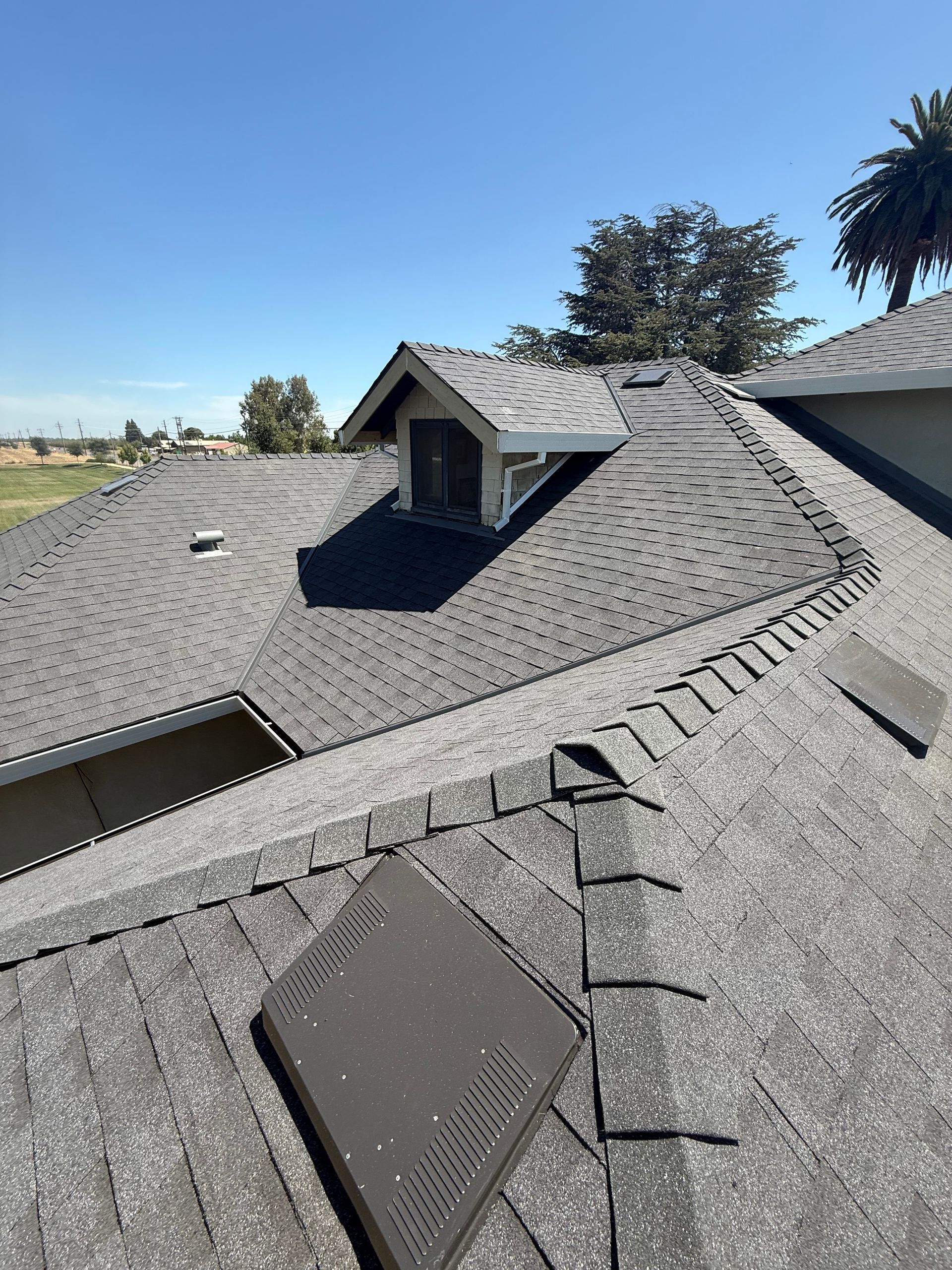 Roof with gray shingles and two dormer windows under a blue sky.