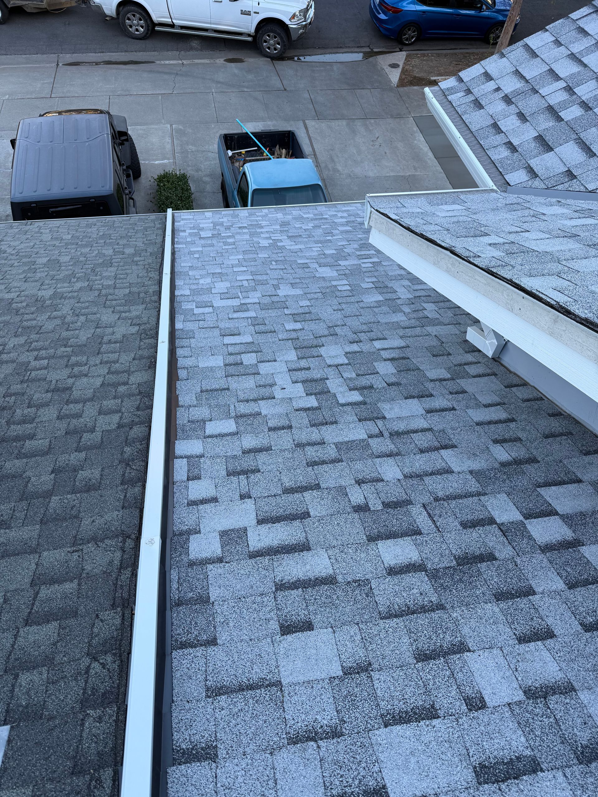 View from a roof with gray shingles overlooking parked cars and a driveway below