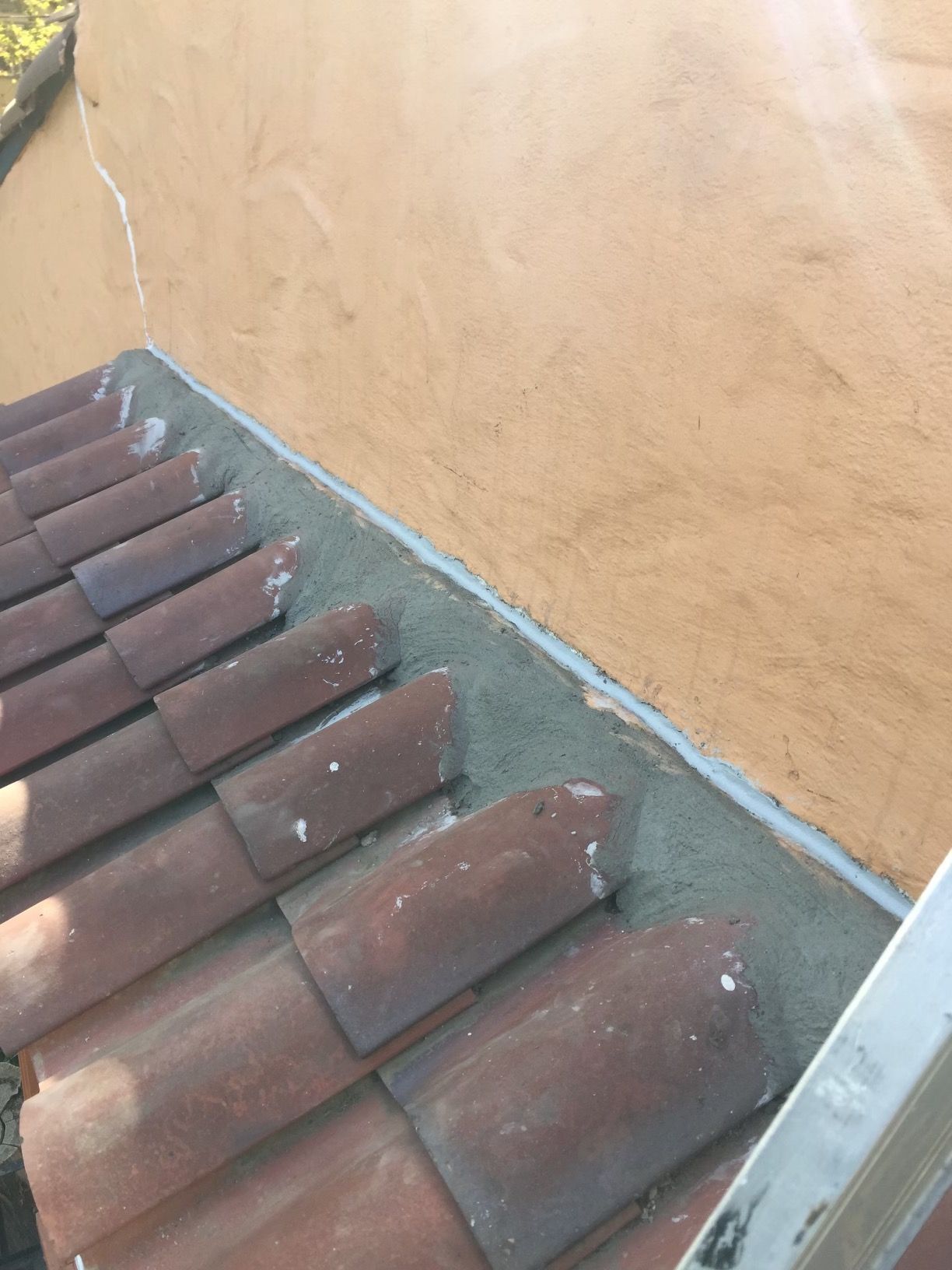 Red roof tiles beside a tan stucco wall, showing a roof edge and gutter.