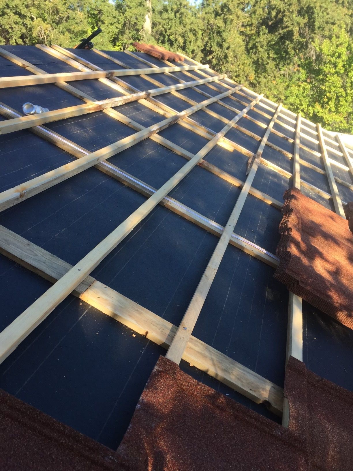 Roof under construction with wooden battens over dark blue panels, seen from above in sunlight