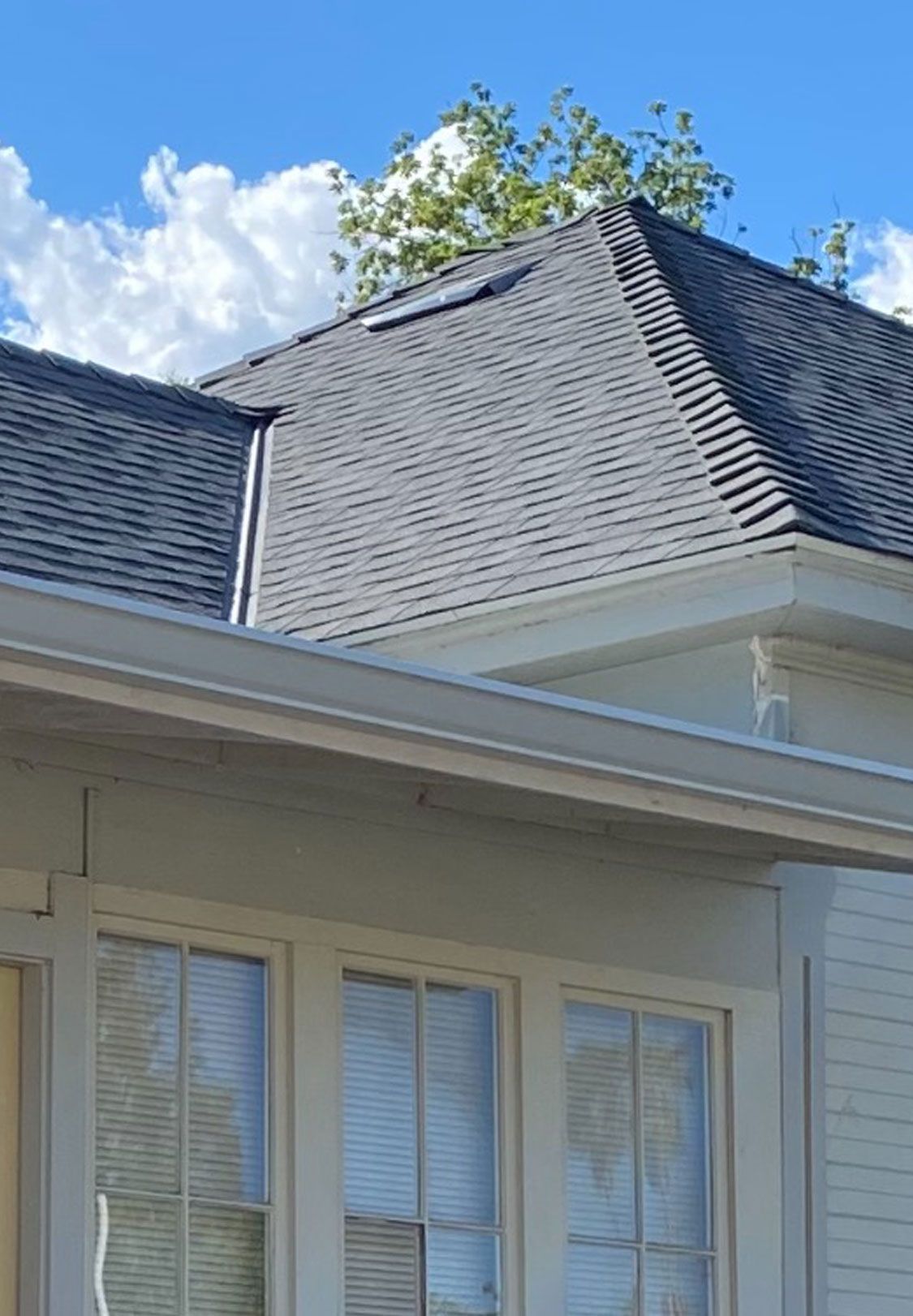 House roof with gray shingles against a blue sky and clouds