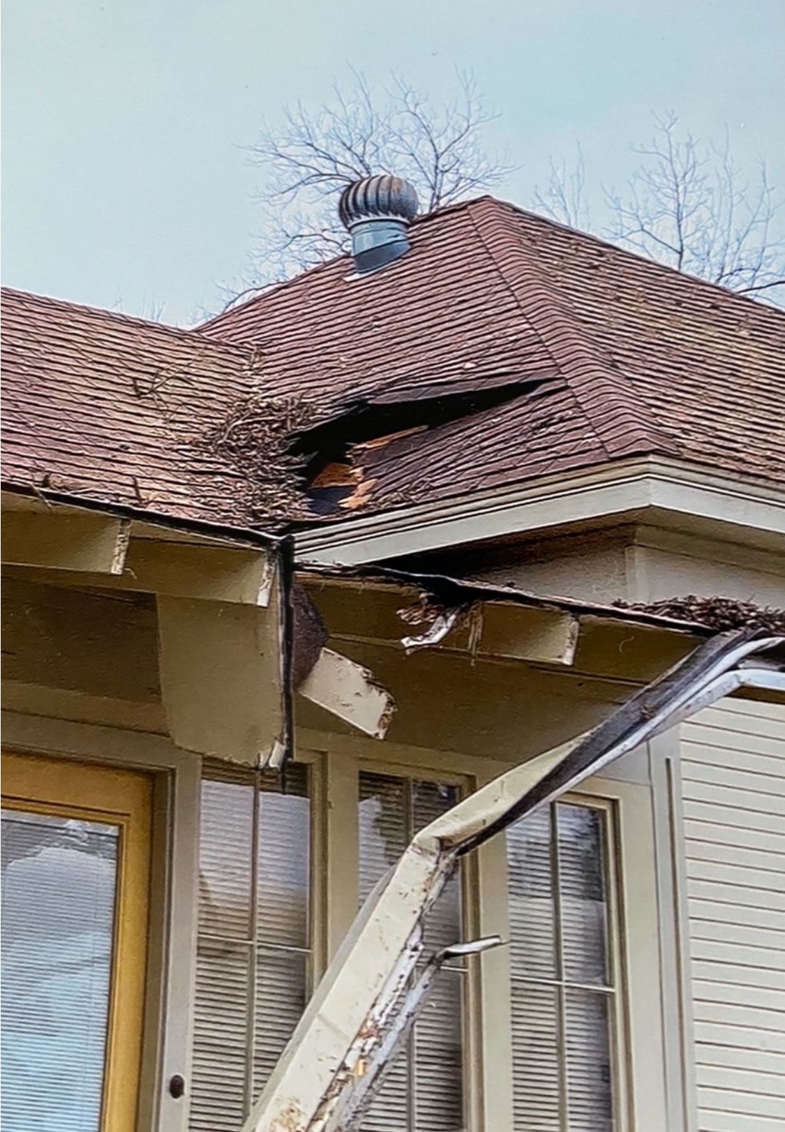 Severely damaged house roof with a large hole and bent siding after storm damage