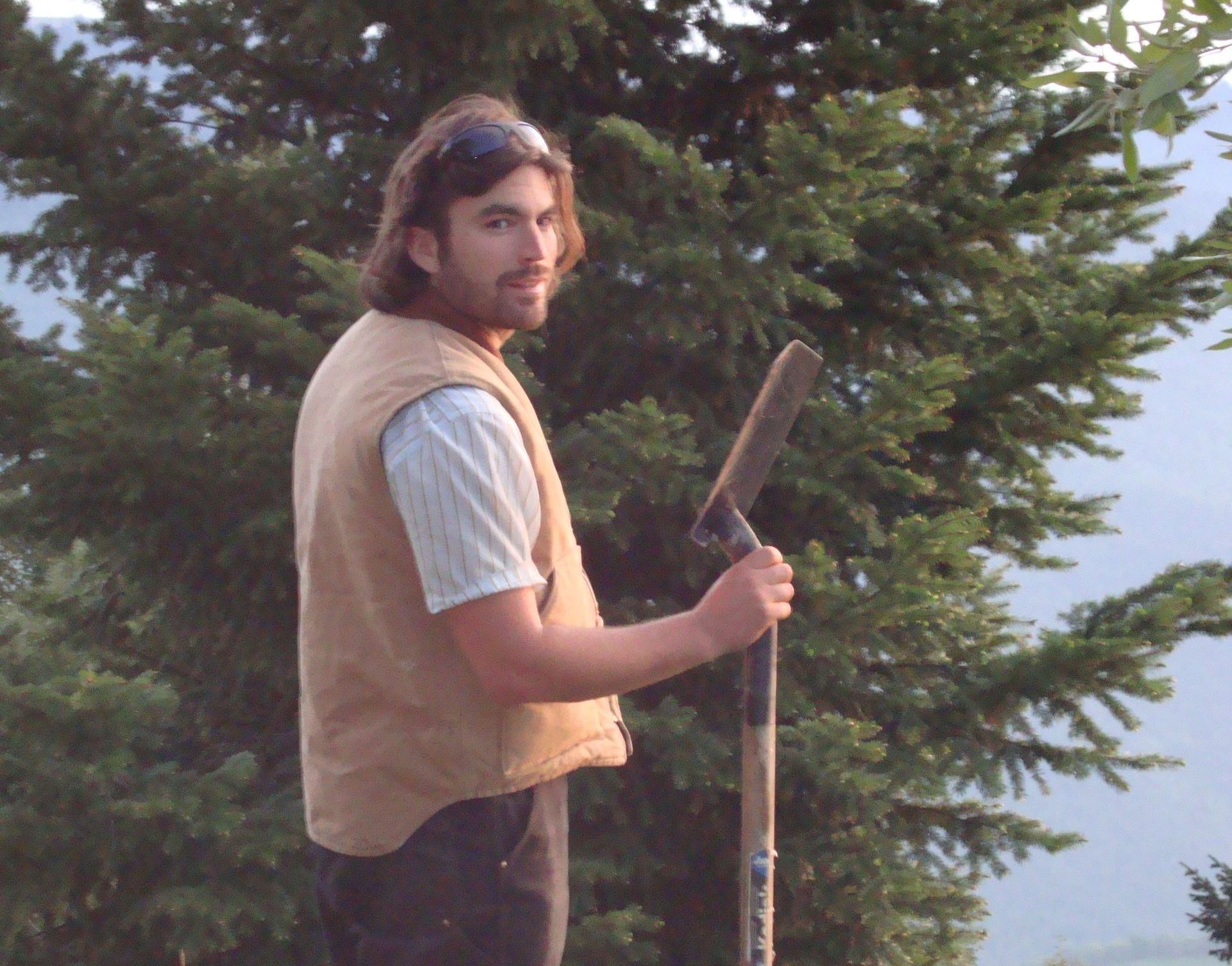A man standing in front of a tree holding a shovel