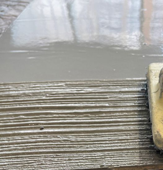 A Person Is Spreading Concrete On A Tile Floor With A Trowel — S & K Gallaway Concreting In West Mackay, QLD