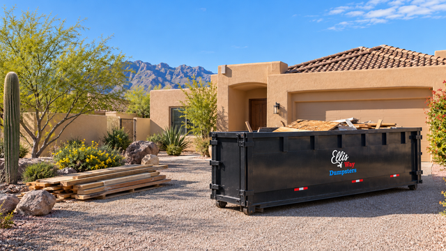 Black dumpster in front of a tan house with desert landscaping and mountains in the background