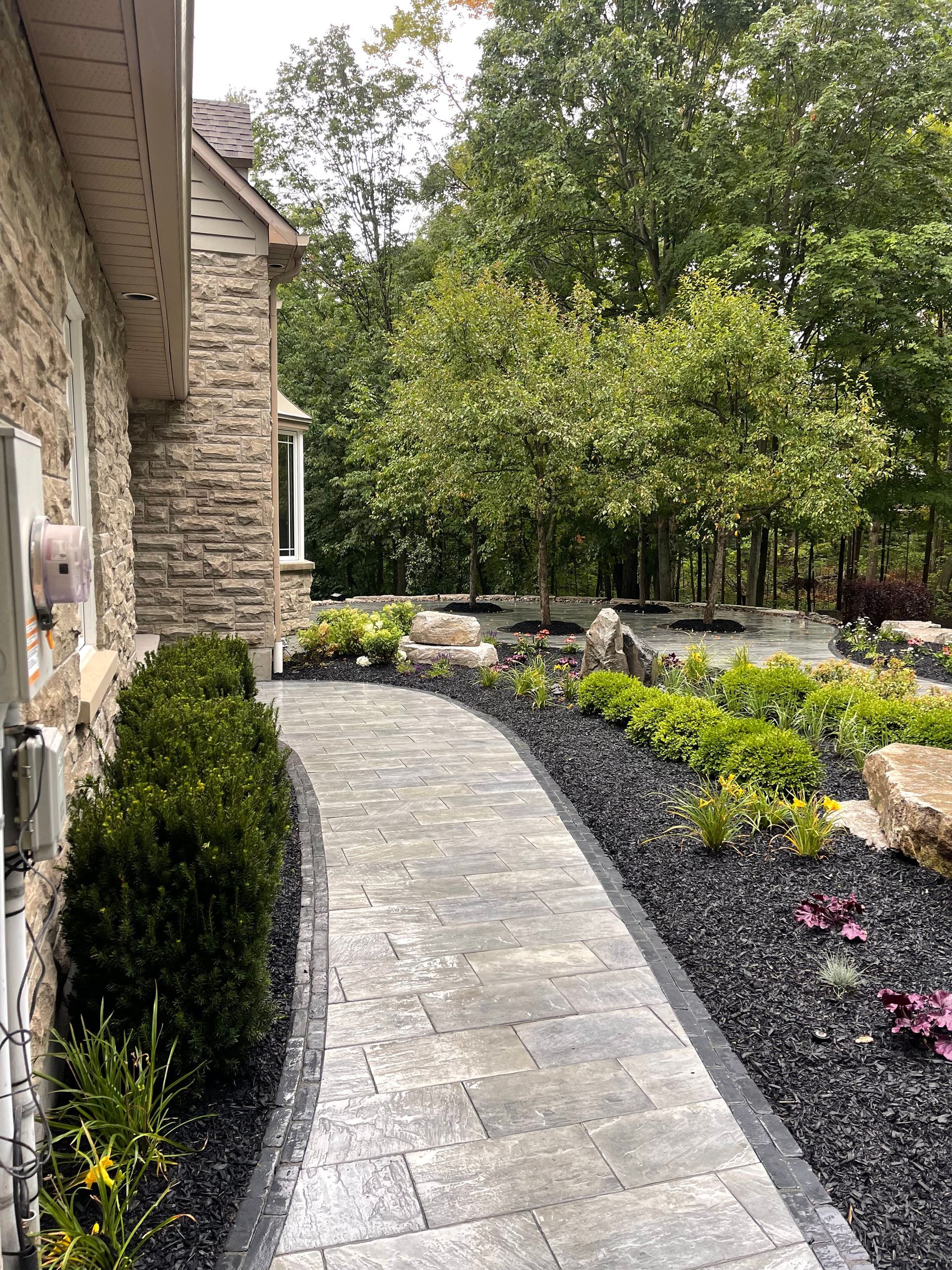A stone walkway leading to a house surrounded by trees and bushes.