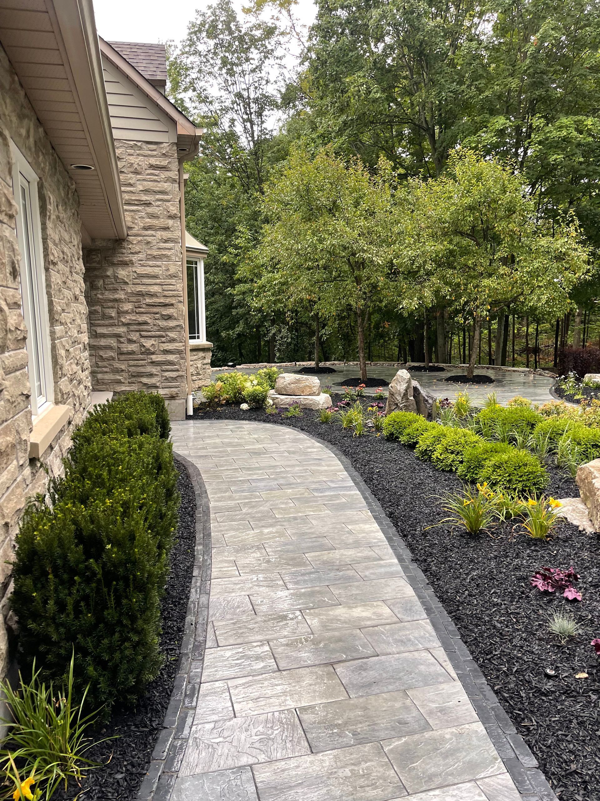 A stone walkway leading to a house surrounded by trees and bushes.
