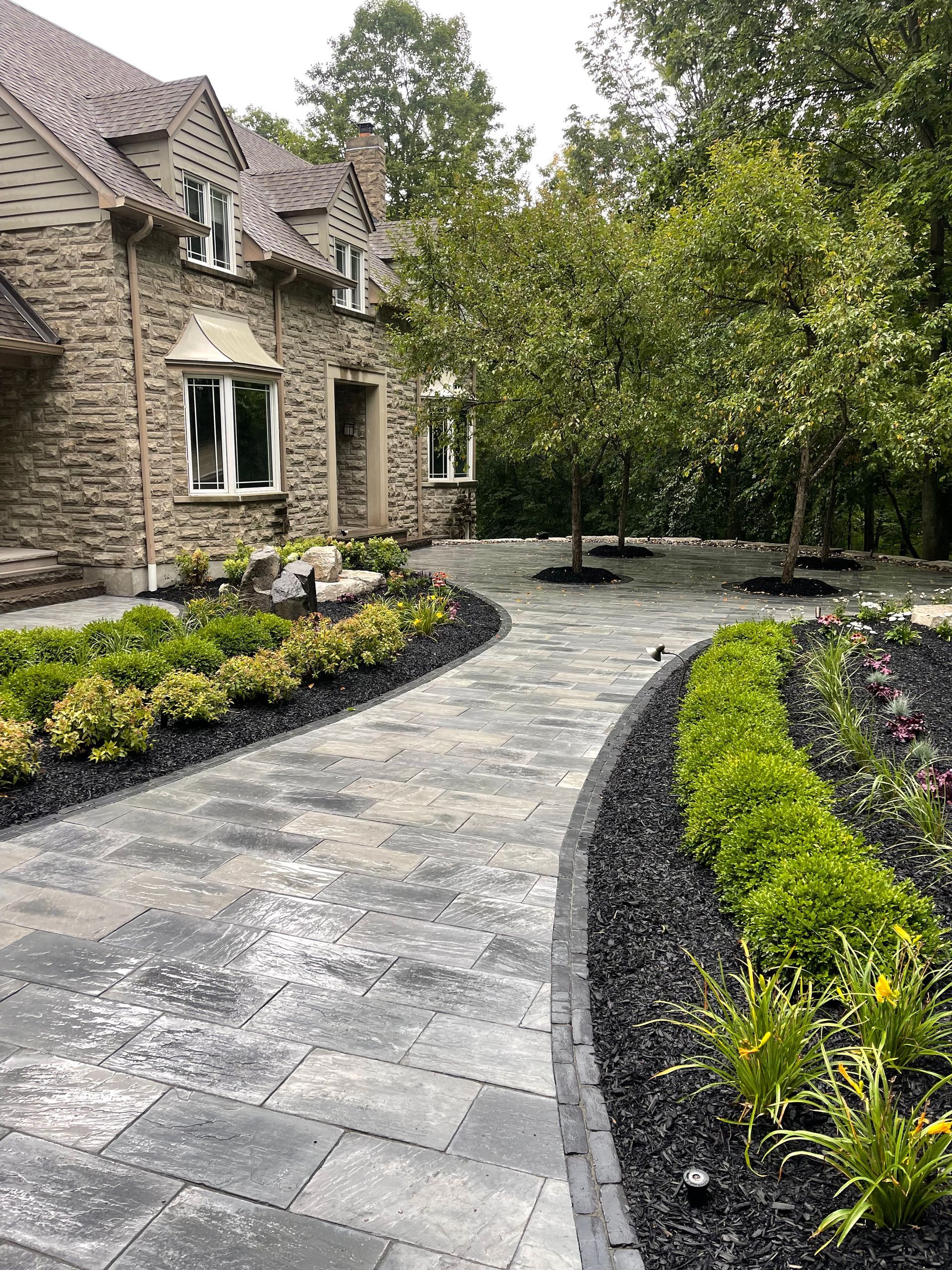 A stone house with a walkway leading to it surrounded by trees and bushes.